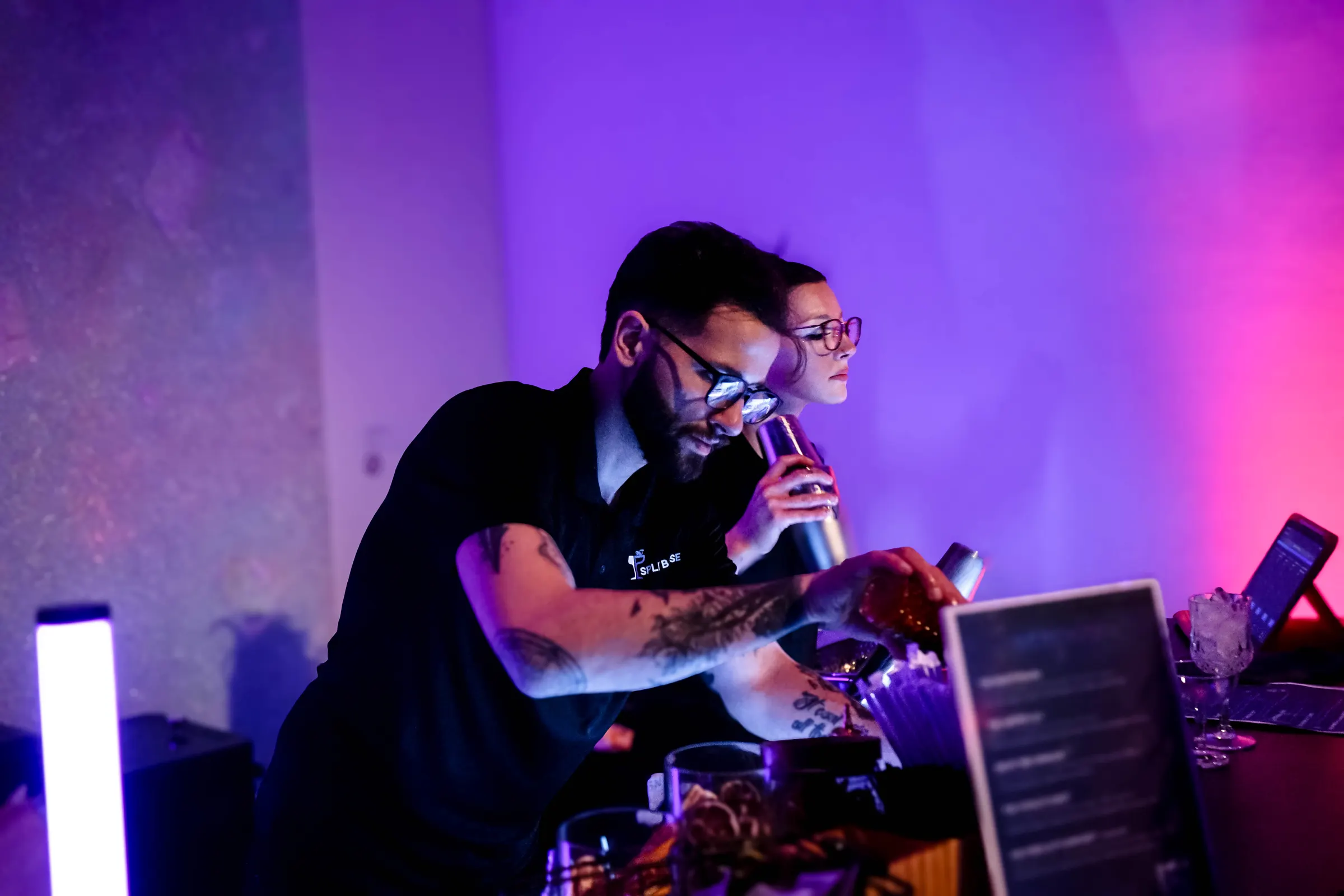 A Split Base bartender building a cocktail under purple event lighting