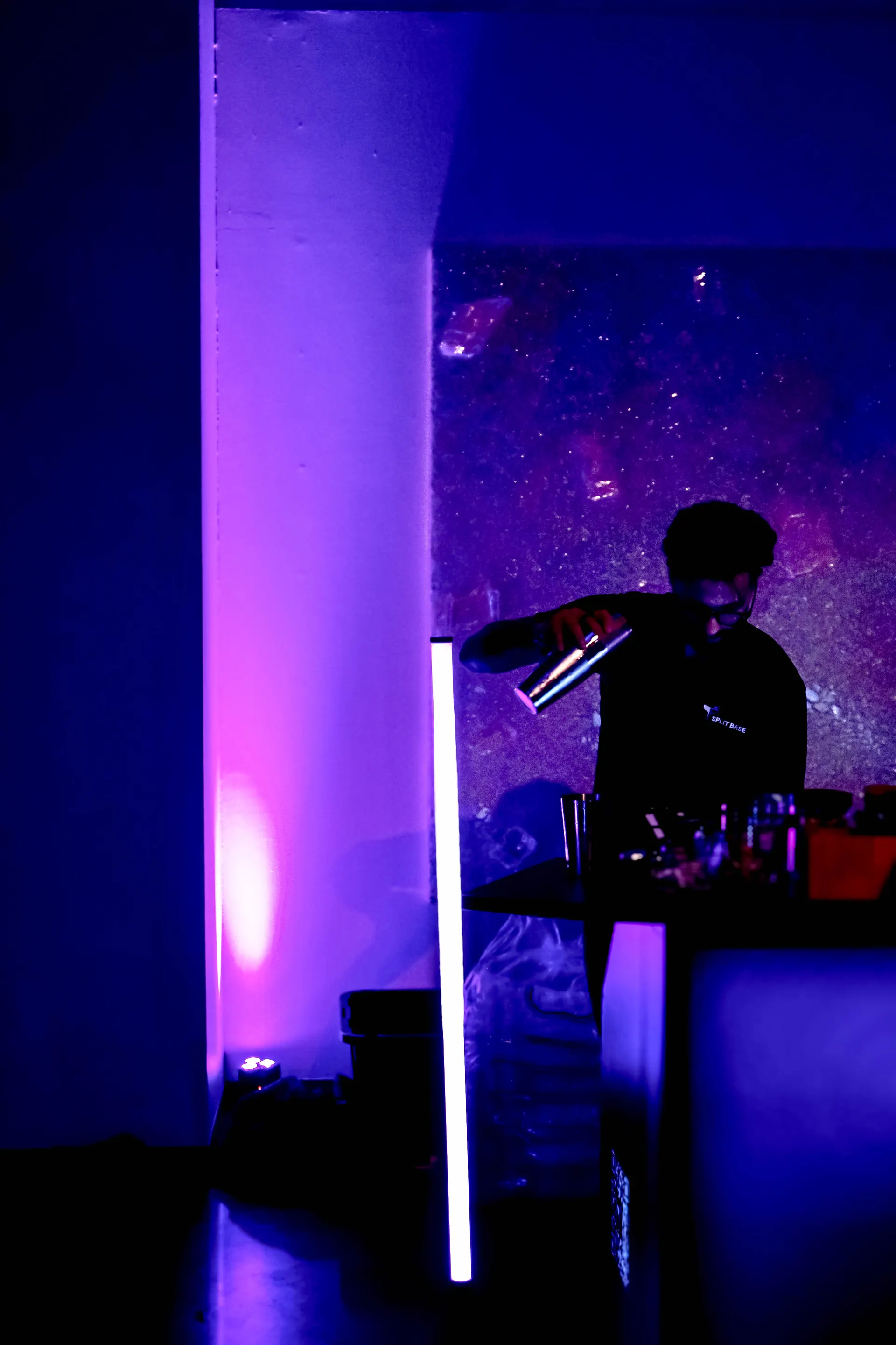 A Split Base bartender silhouetted mid-pour under purple event lighting